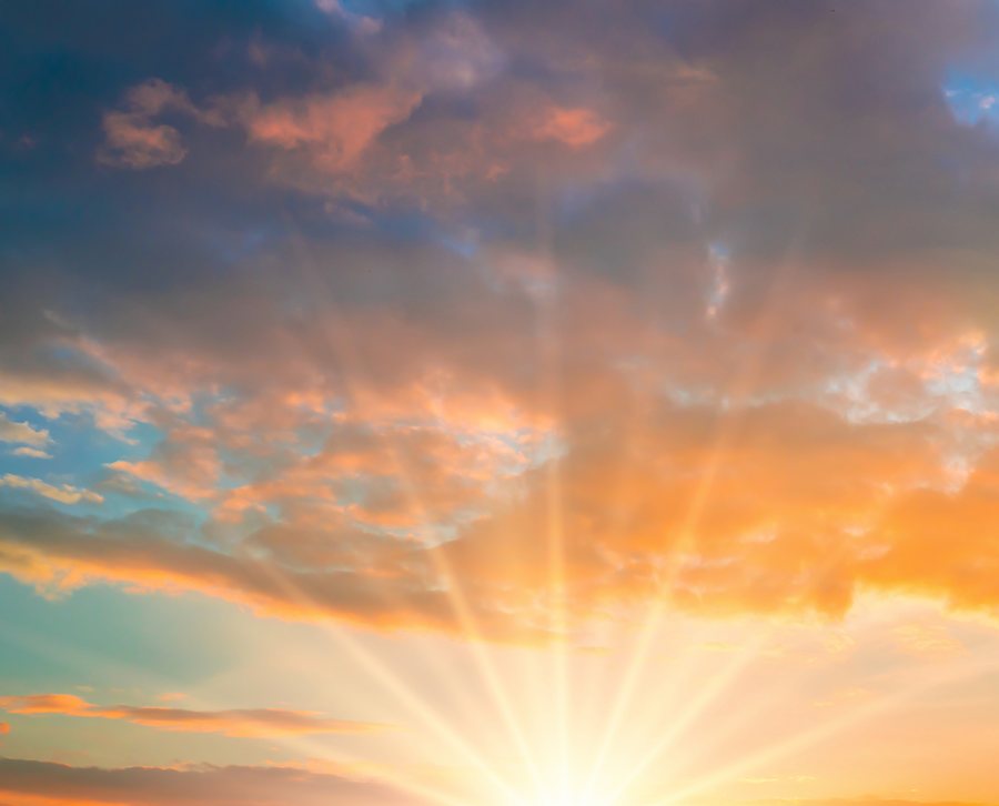 The sun rising on the horizon, its rays breaking up through the clouds.
